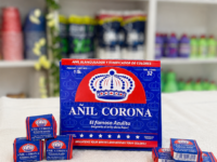 Caja de Añil Corona, el famoso jabón azulito, junto a cubitos individuales sobre un mantel blanco, en exhibición de tienda